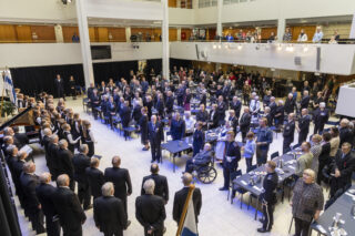 Ihmisiä seisomassa hallissa, jonka pöydille on katettu kahviastioita